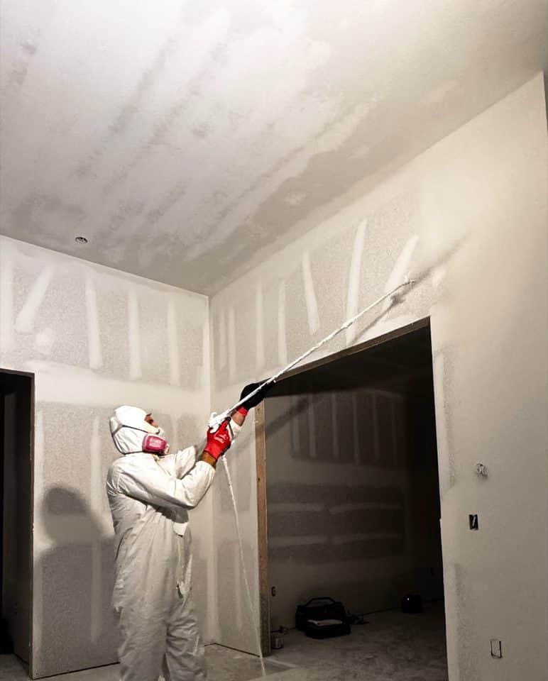 Spraying drywall primer in white coveralls | new home construction in Port Charlotte, FL by Sosnin Builders