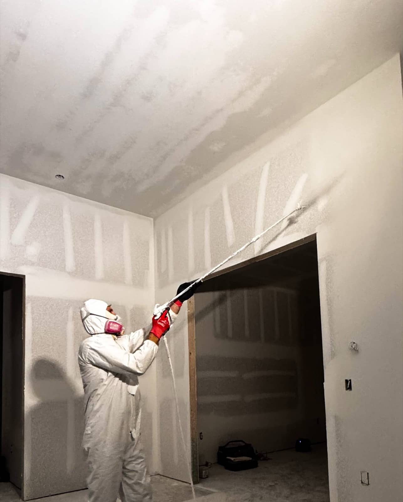 Spraying drywall primer in white coveralls | new home construction in Port Charlotte, FL by Sosnin Builders