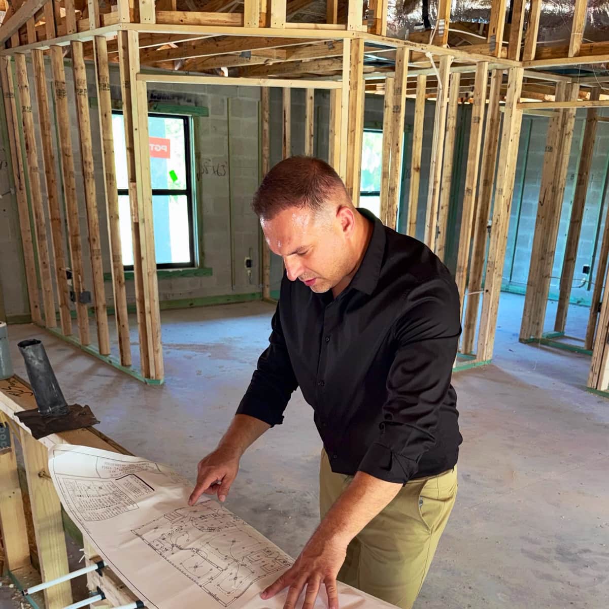 Tony Sosnin reviewing construction plans inside a framed home